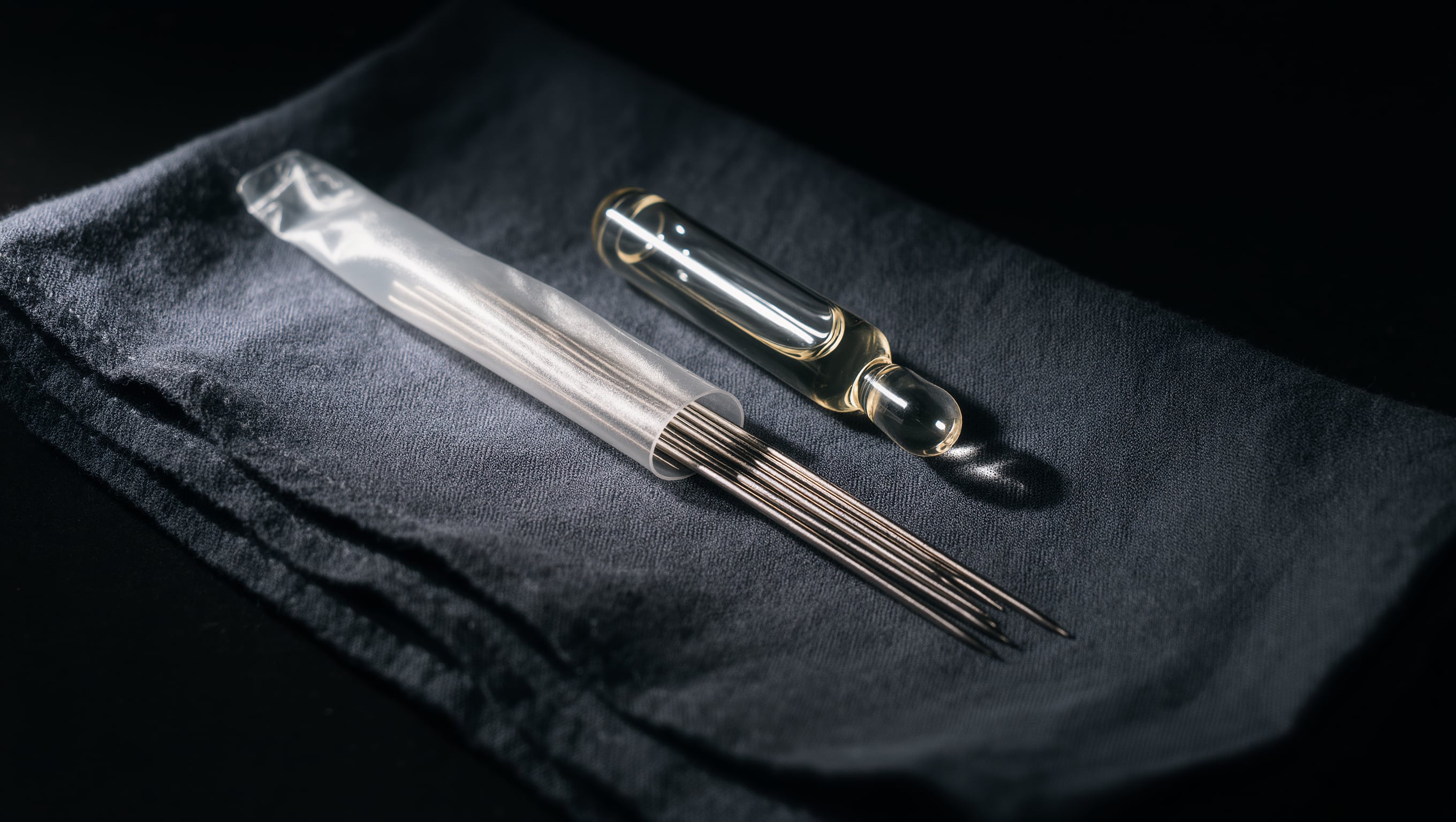 Eine sterile Nadelkartusche in Nahaufnahme neben einer verschlossenen Ampulle auf dunklem Tuch, kaltes Licht auf dem Metall